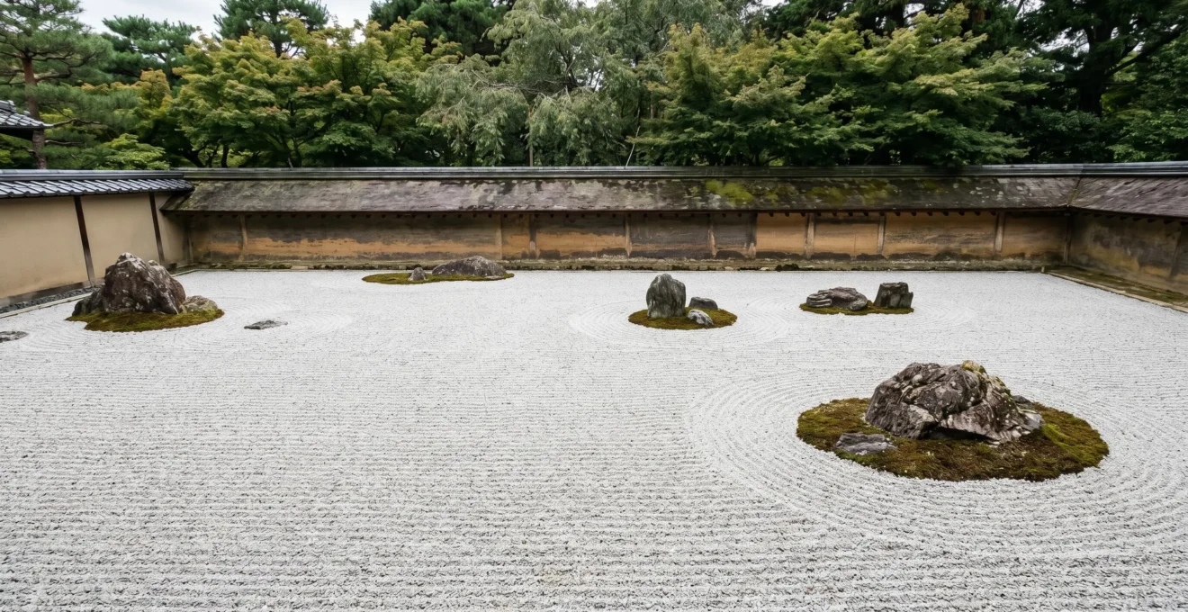 Jardin zen japonais avec gravier blanc ratissé en motifs ondulants autour de rochers, illustrant la philosophie de contemplation