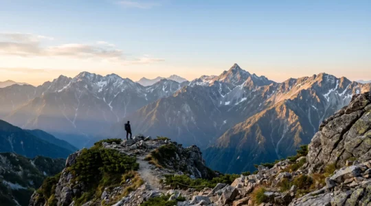 Vue panoramique des sommets enneigés des Alpes japonaises avec un randonneur contemplant la vallée de Kamikochi depuis un sentier de crête au lever du soleil